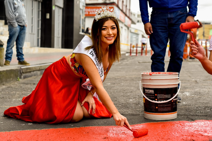 Reina del Carnaval de Negros y Blancos pintando una cebra color rojo en una vía